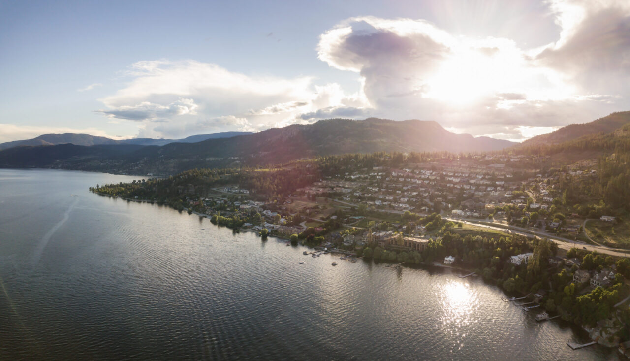 Aerial view of lakeside neighbourhoods and forested hills in the Okanagan.