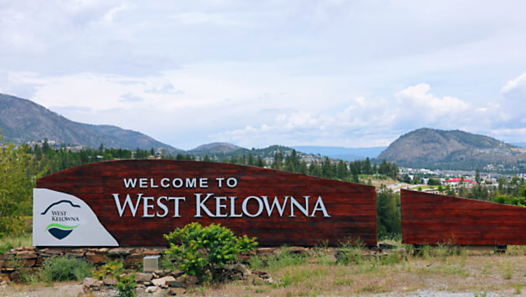Welcome to West Kelowna sign with mountains in the background.