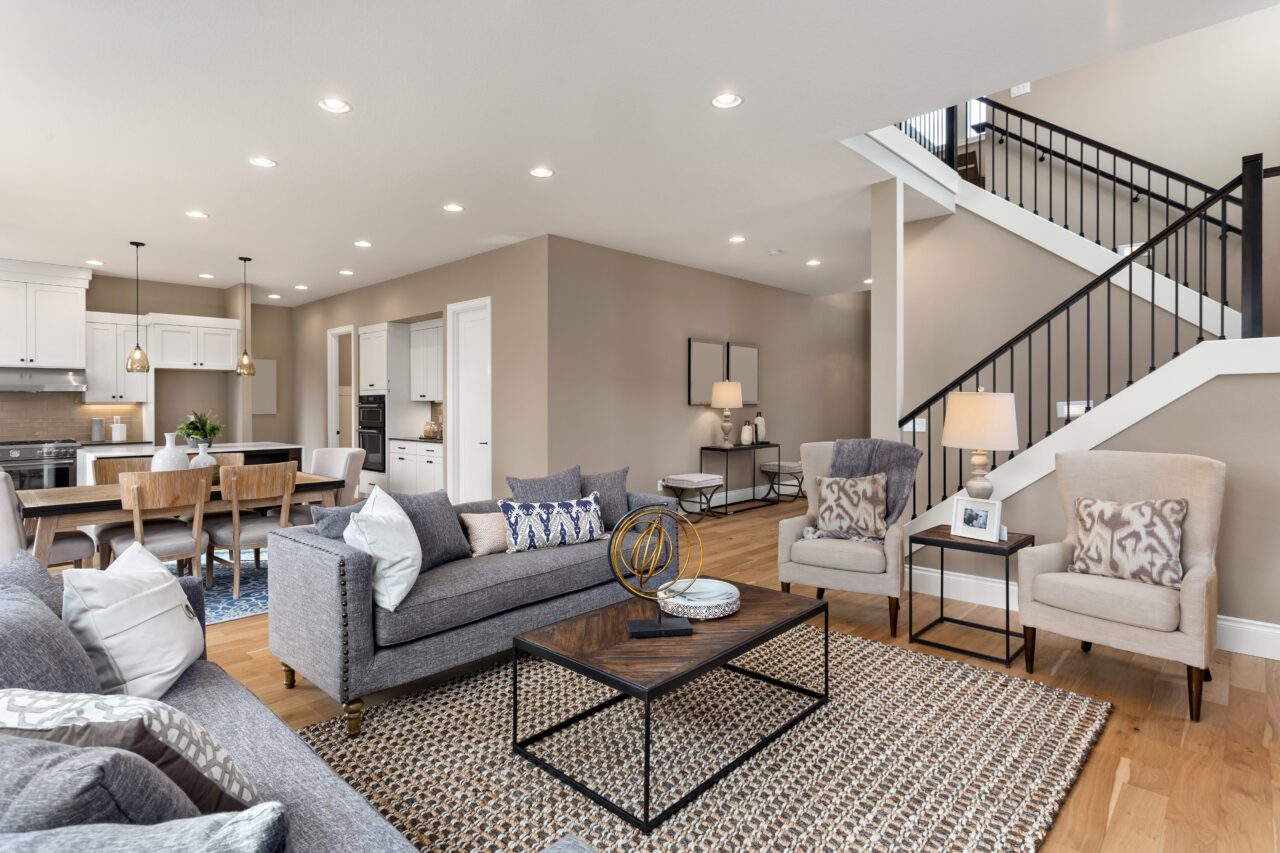 Living room with grey seating, an open kitchen, and a staircase to the upper floor.