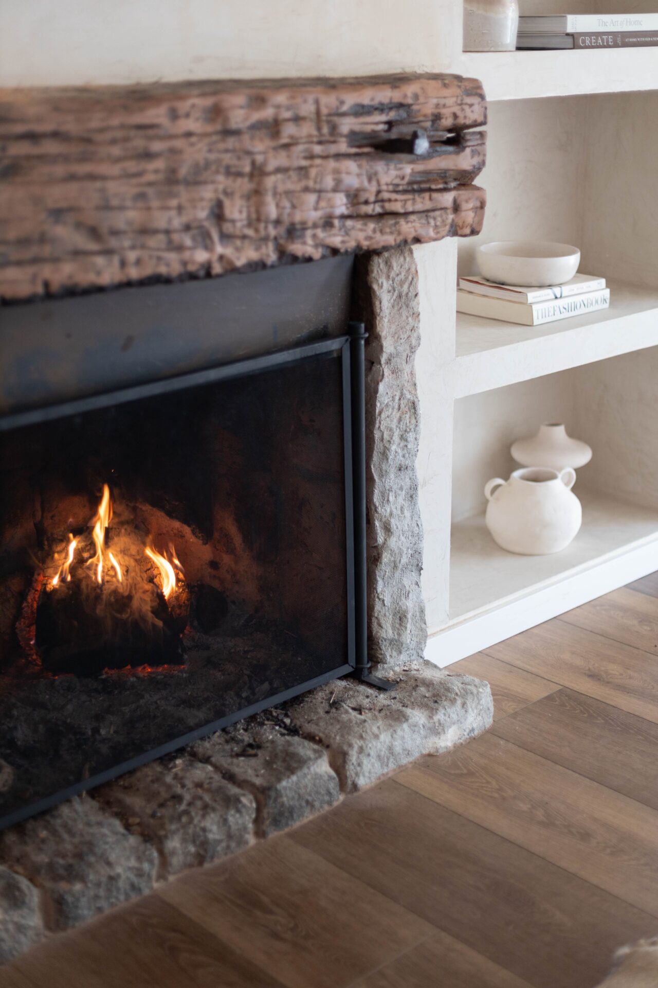 Lit stone fireplace with a rustic wood mantel and white shelving.